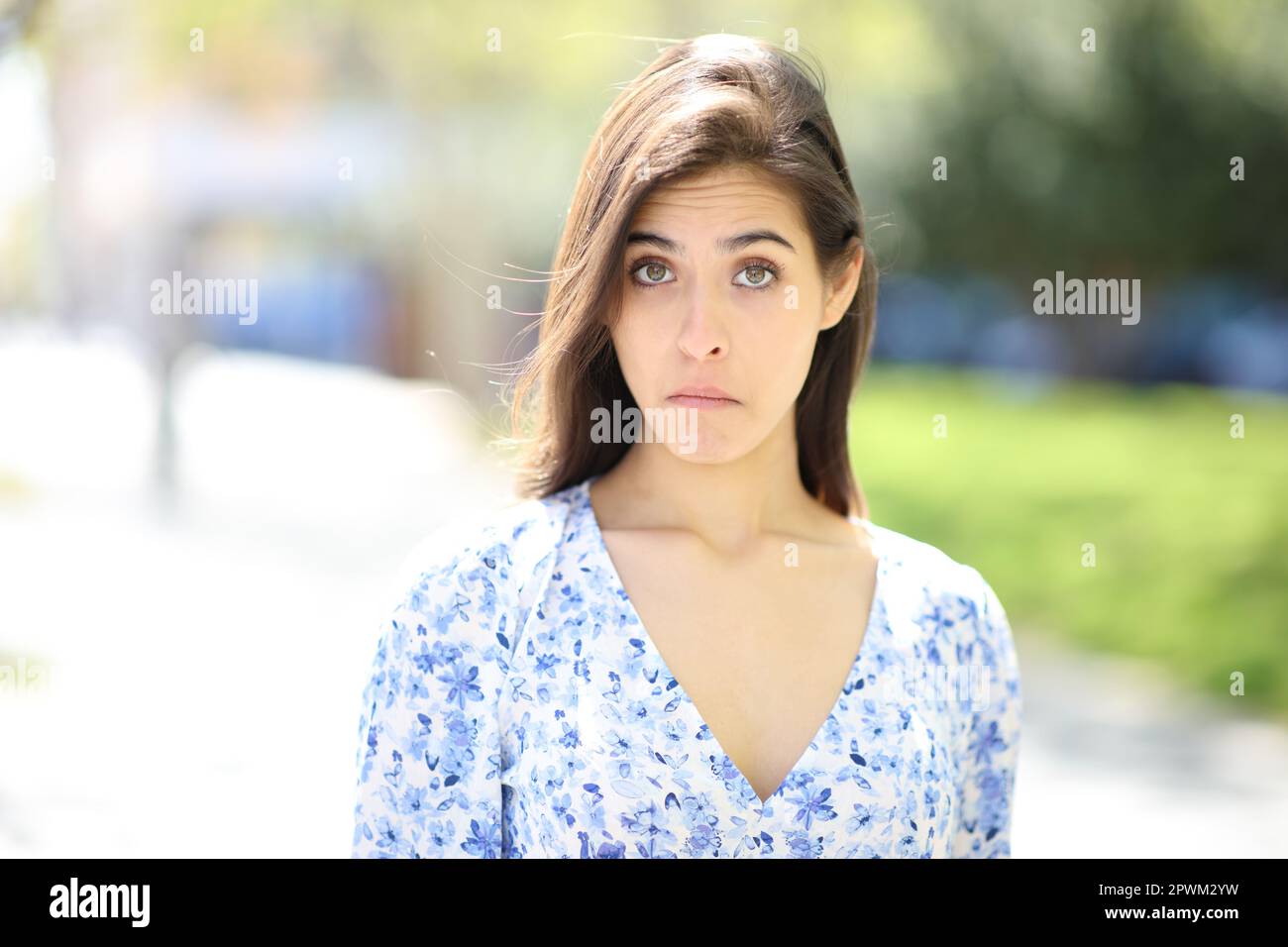 Vista frontale ritratto di una donna perplessa che guarda la fotocamera in strada Foto Stock