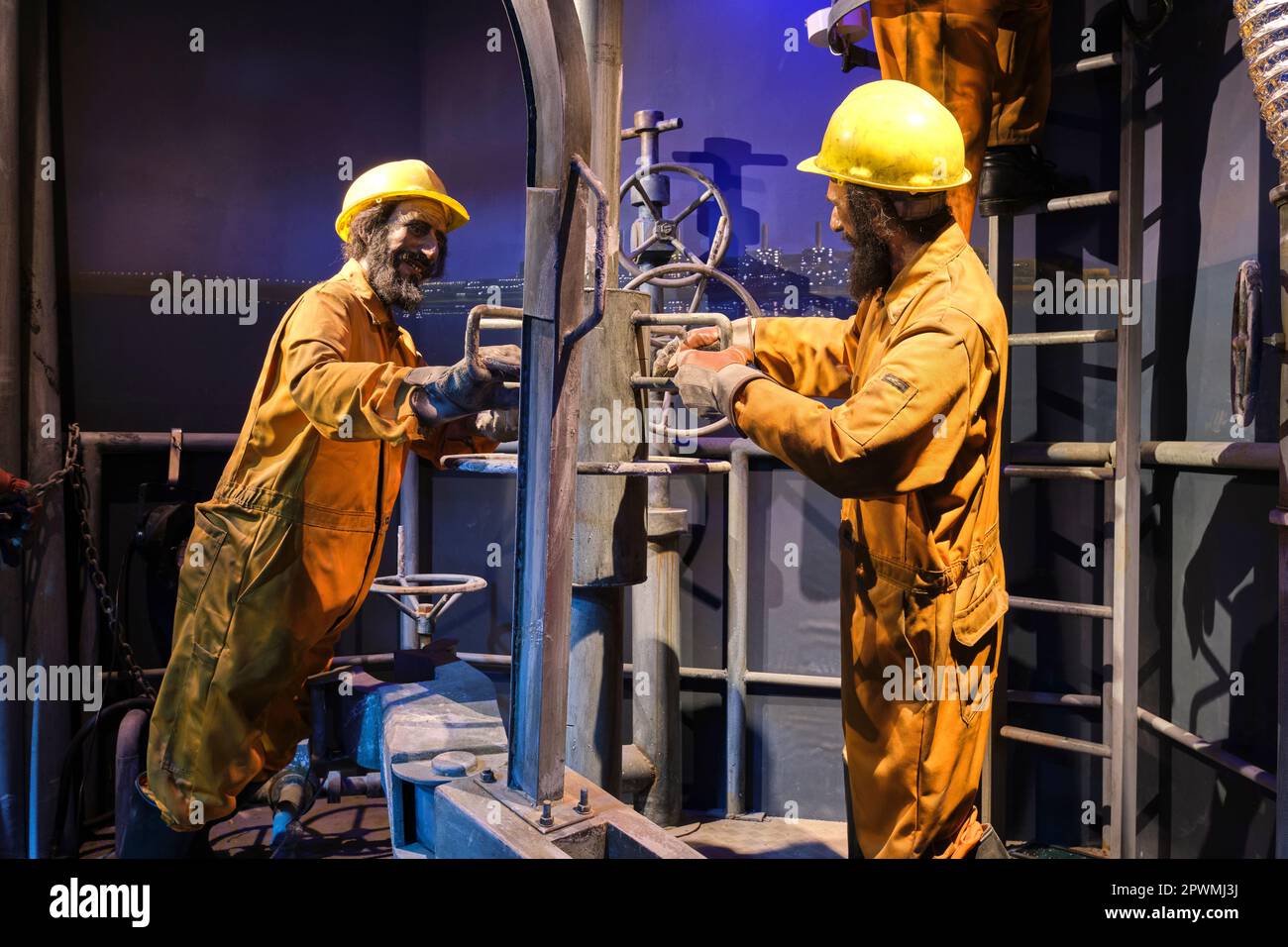 Un gruppo di petrolieri, derick, lavoratori di pozzi in tute arancioni, impegnati a regolare un tubo di perforazione. Un diorama raffigurante una scena del passato degli Emirati Arabi Uniti, all'Abu Foto Stock
