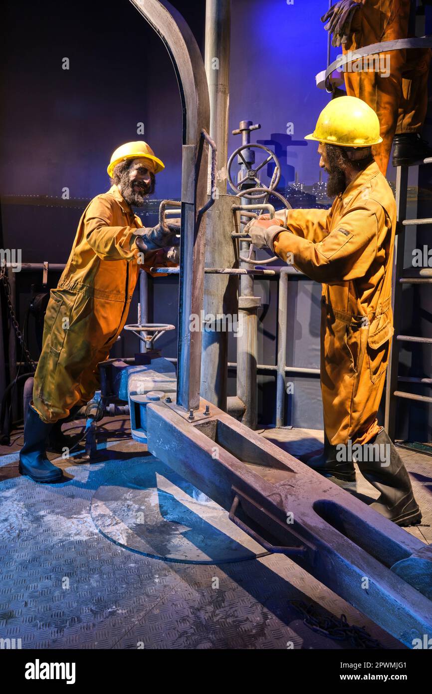 Un gruppo di petrolieri, derick, lavoratori di pozzi in tute arancioni, impegnati a regolare un tubo di perforazione. Un diorama raffigurante una scena del passato degli Emirati Arabi Uniti, all'Abu Foto Stock