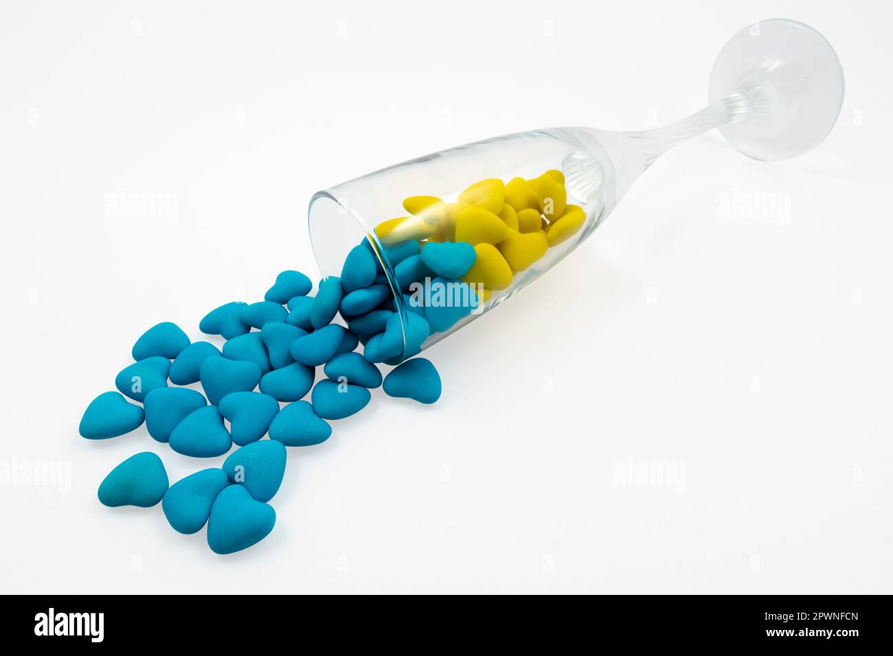 Vetro rovesciato con caramelle a forma di cuore gialle e blu (primo piano) isolate su sfondo bianco. Simboli di Stato dell'Ucraina. Vista dall'alto Foto Stock