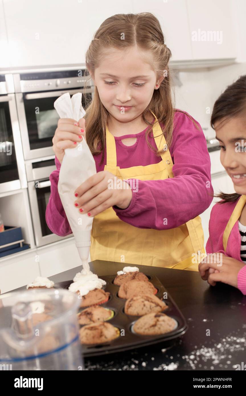 La glassa della scolaretta sui muffin con il sacchetto della glassa nella classe domestica di economia, Baviera, Germania Foto Stock