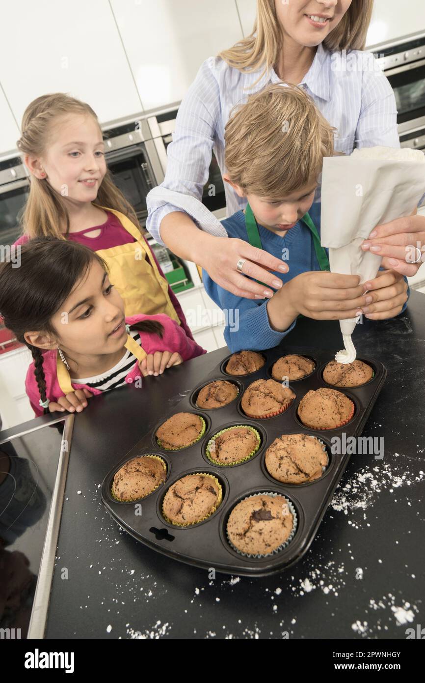 La glassa del ragazzo di scuola sui muffin con il sacchetto della glassa nella lezione domestica di economia, Baviera, Germania Foto Stock