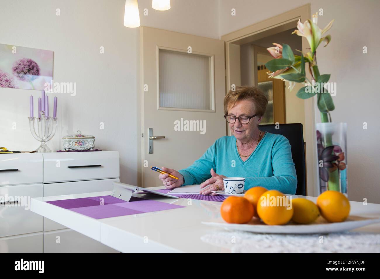 Vecchia donna che scrive nel libro al tavolo da pranzo Foto Stock