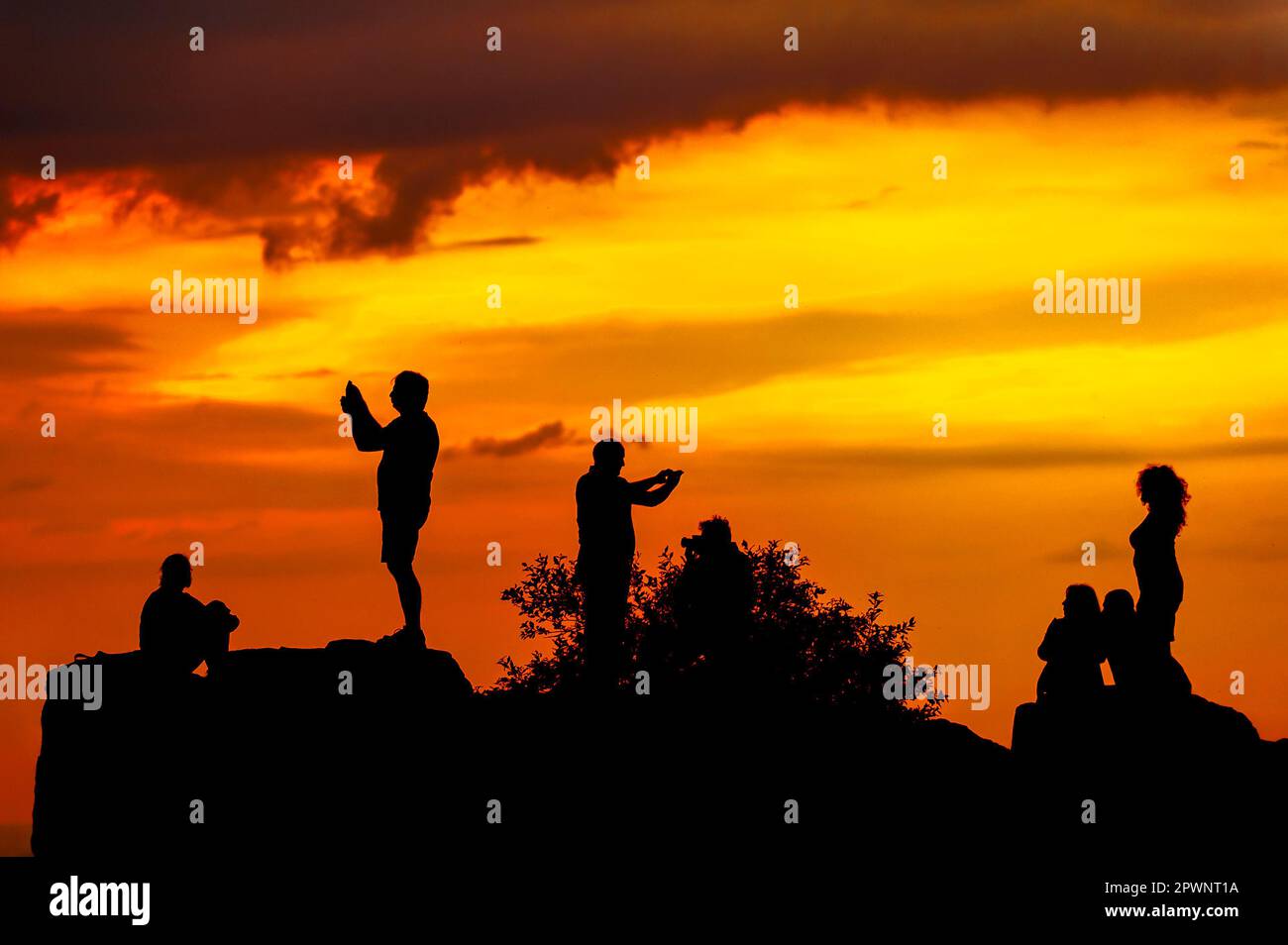 Silhouette di persone sul rock scattare foto e selfie su sfondo arancione cielo Foto Stock