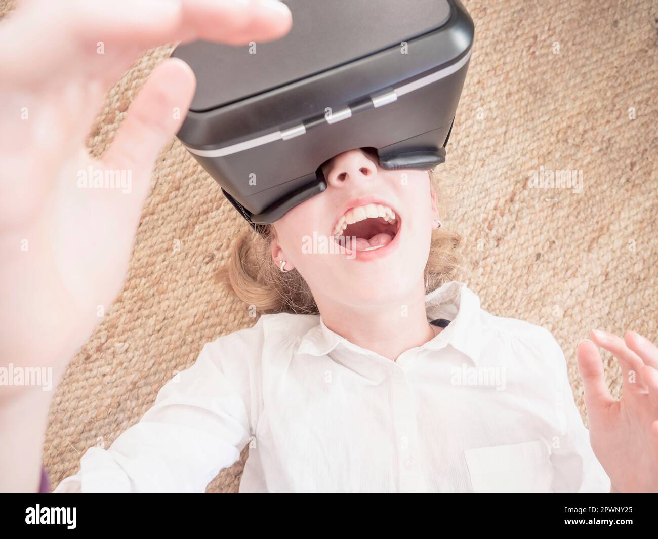 Ragazza che usa cuffie per realtà virtuale mentre si trova sul pavimento Foto Stock