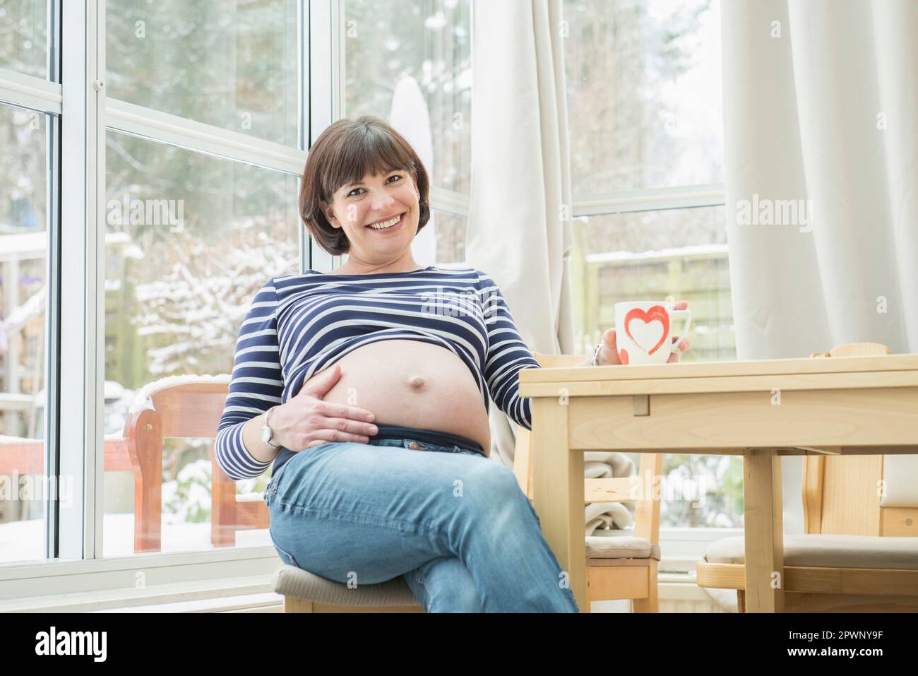 Ritratto di donna incinta seduta su sedia Foto Stock