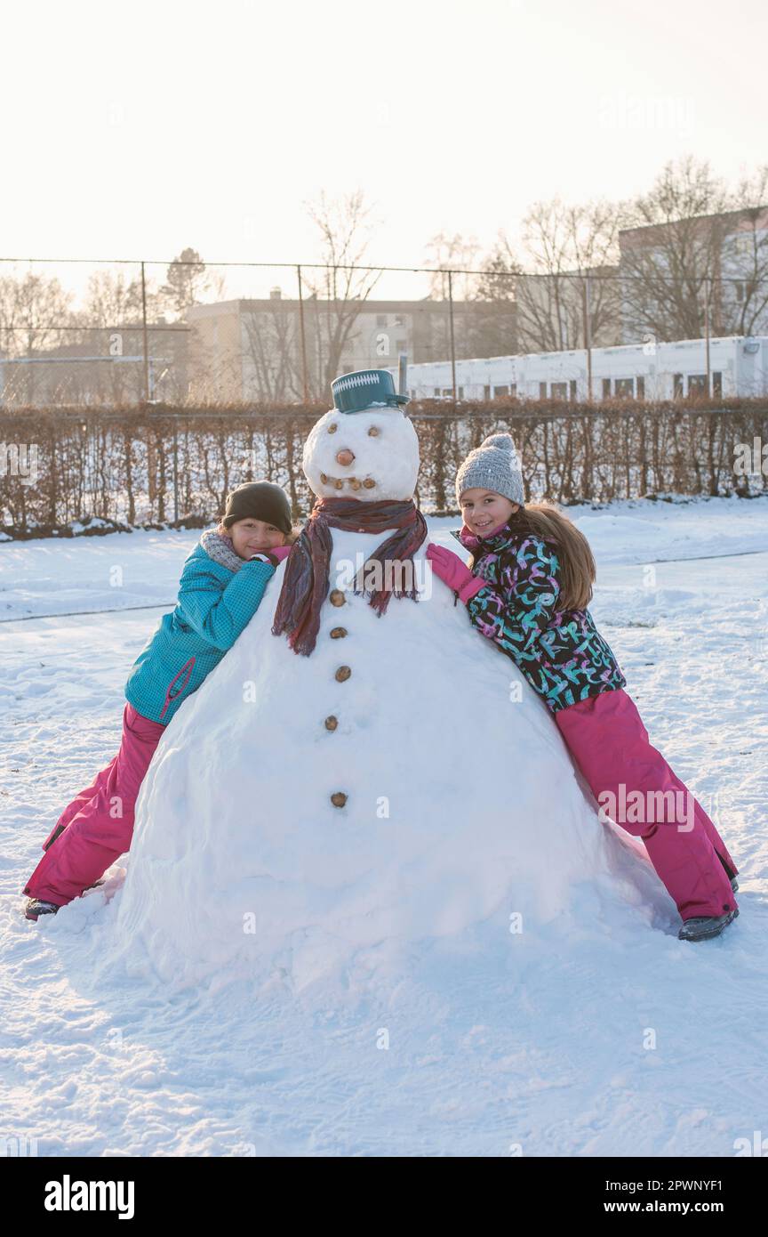 Due ragazze appoggiate sul pupazzo di neve sul campo di neve Foto Stock