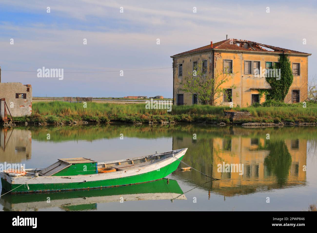 Barca verde sullo sfondo del riflesso di una vecchia casa nel Delta del po in Italia in un chiaro giorno di maggio. Foto Stock