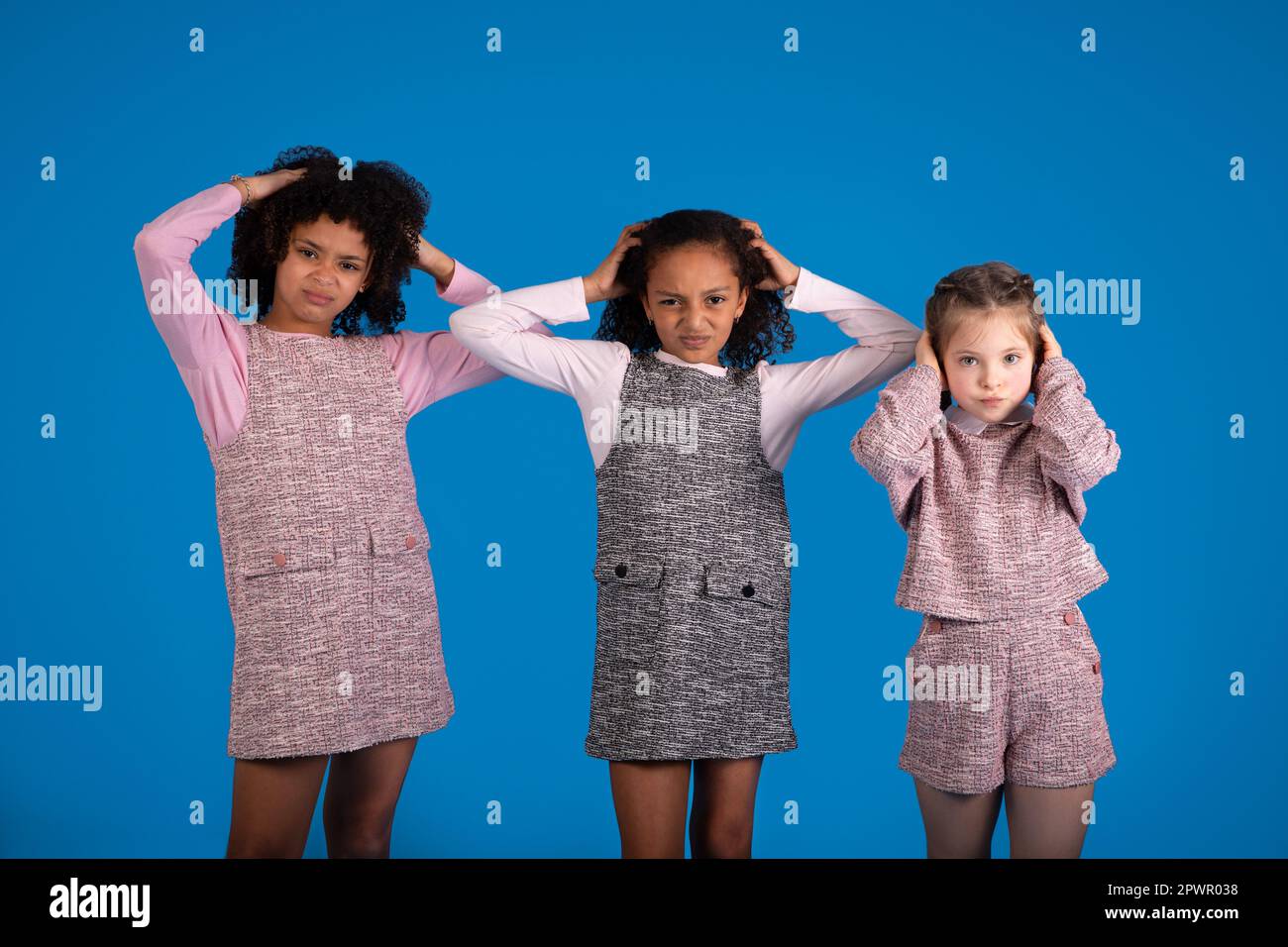 Ragazze internazionali tristi in casual copre le orecchie, soffrono di rumore isolato su sfondo blu Foto Stock