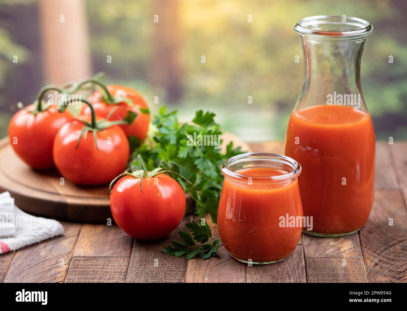 Succo di pomodoro in vetro e caraffa con pomodori freschi e prezzemolo su tavolo di legno con sfondo estivo Foto Stock