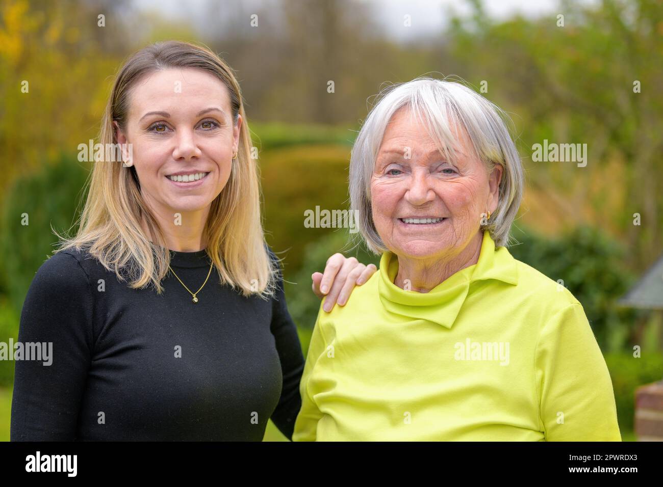 Famiglia di due generazioni, madre e figlia, la figlia ha la mano sulla spalla della madre guardando amichevole la fotocamera Foto Stock