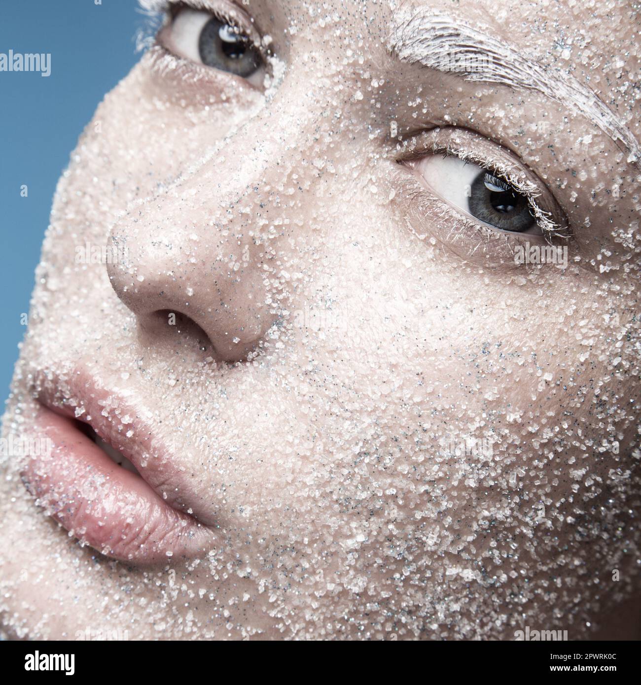 Ritratto di una ragazza con pelle pallida e neve di zucchero sul viso. Arte creativa bellezza moda. Foto scattata in studio su sfondo blu. Foto Stock