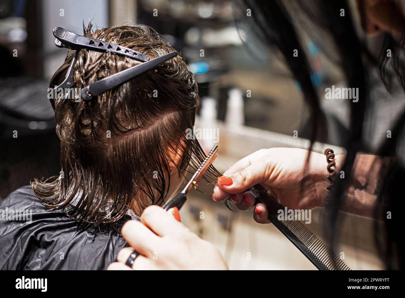 barbiere taglia sotto il coltello le punte di capelli puliti bagnati ad un adolescente Foto Stock