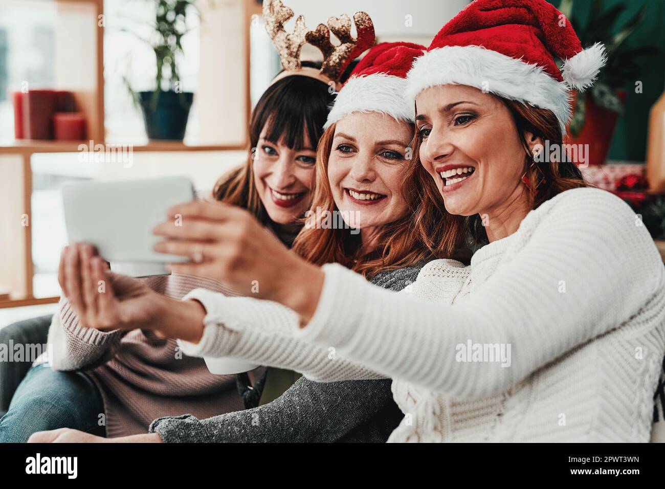Questa è l'ultima foto che prometto. Tre attraenti donne di mezza età che scattano autoritratti insieme a un cellulare a casa durante il periodo natalizio Foto Stock