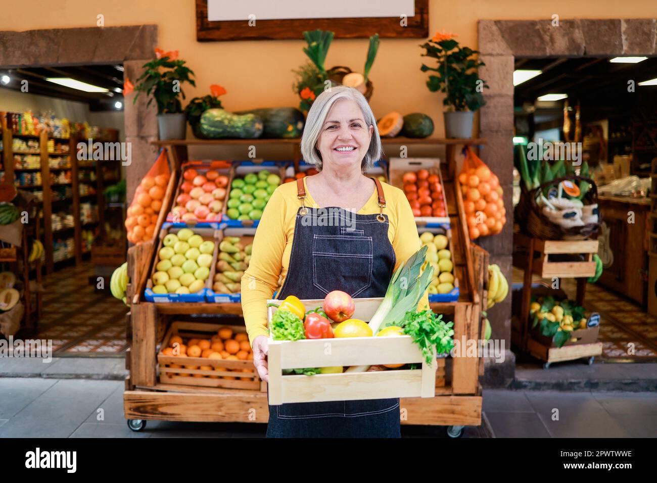 Agriculture shop - Senior woman che lavora al market store, tenendo in mano verdure biologiche scatola di legno - Green business concept Foto Stock