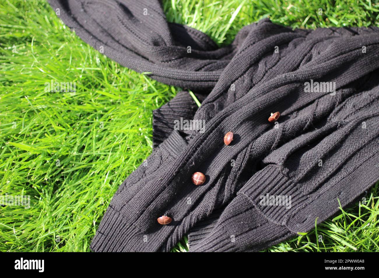 Cardigan nero lavorato a maglia con bottoni di legno disposti su una collina verde erba Foto Stock