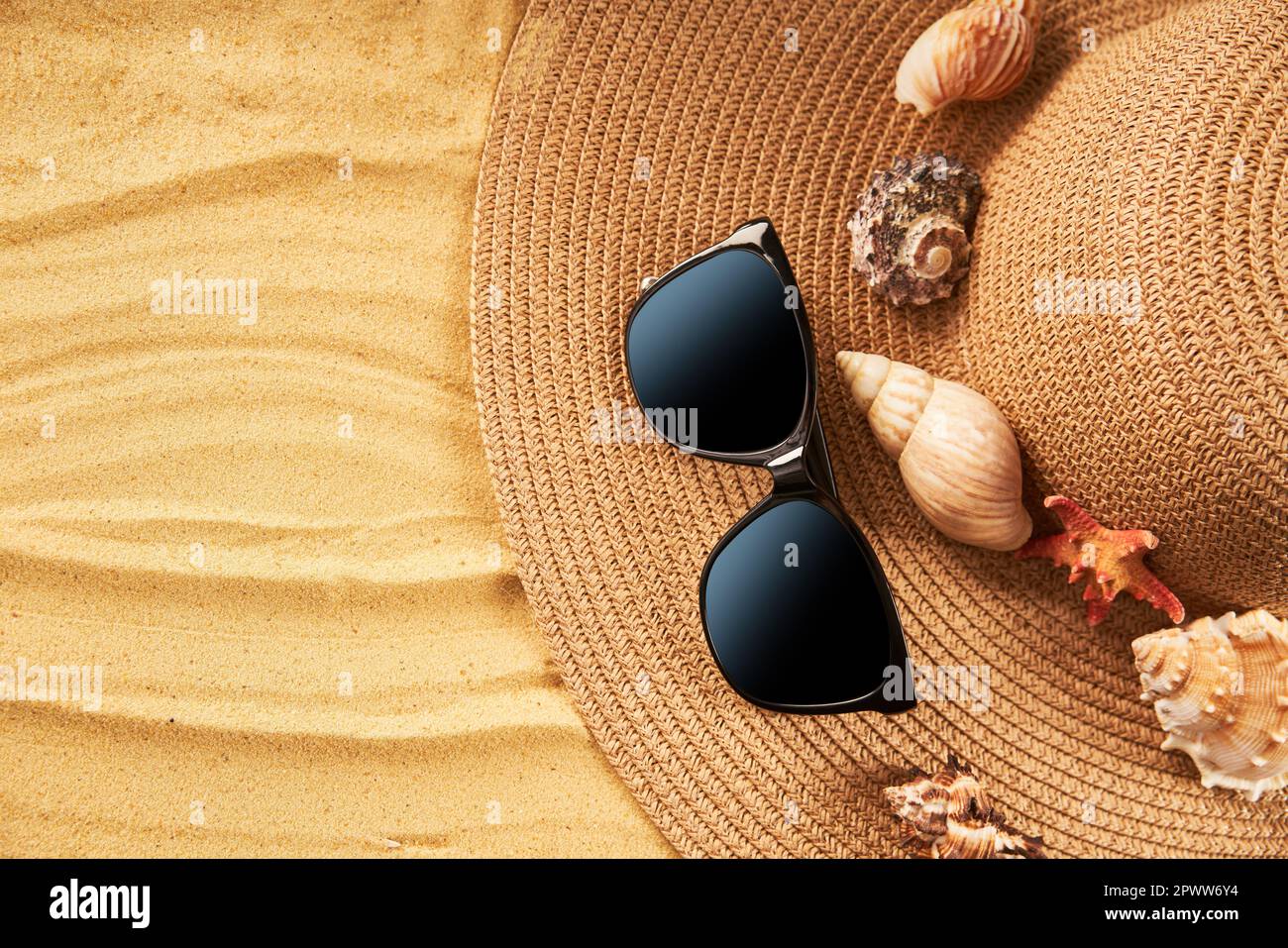Vacanza estiva concetto. Cappello di paglia, occhiali da sole e conchiglie sulla spiaggia di sabbia con spazio per il testo. Piano di giacitura, vista dall'alto Foto Stock