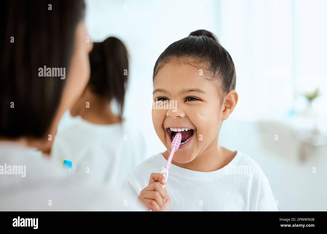 Spazzolare anche la lingua. una adorabile bambina che le sfrega i denti mentre sua madre la aiuta a casa Foto Stock