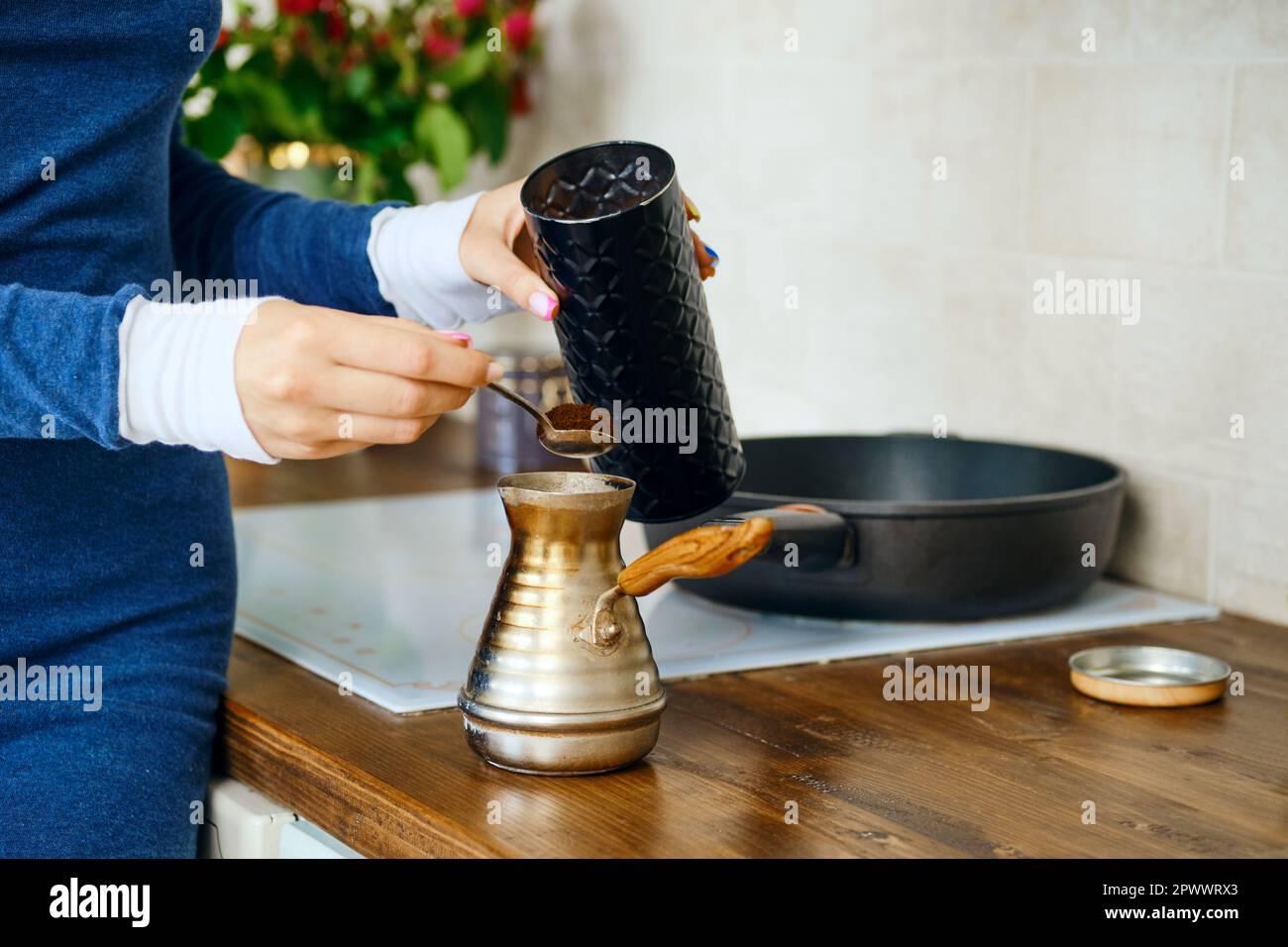 Primo piano della mano femminile con cucchiaio con caffè macinato vicino a una turca. Preparazione del caffè in pentola di metallo. Foto Stock