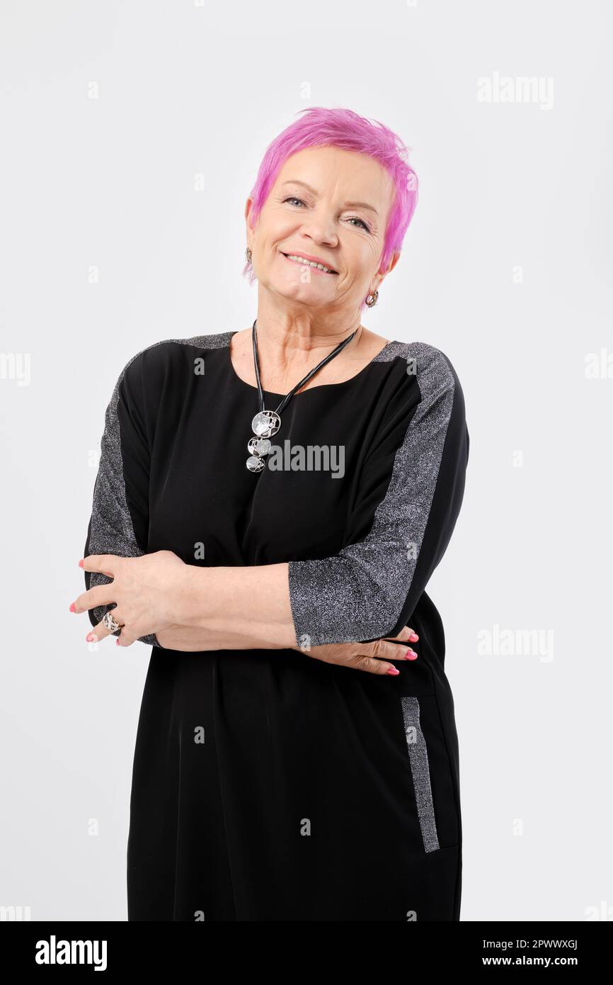 Sorridente vecchia donna con corti capelli rosa tiene le mani incrociate. Concetto di emozione positiva. Foto Stock