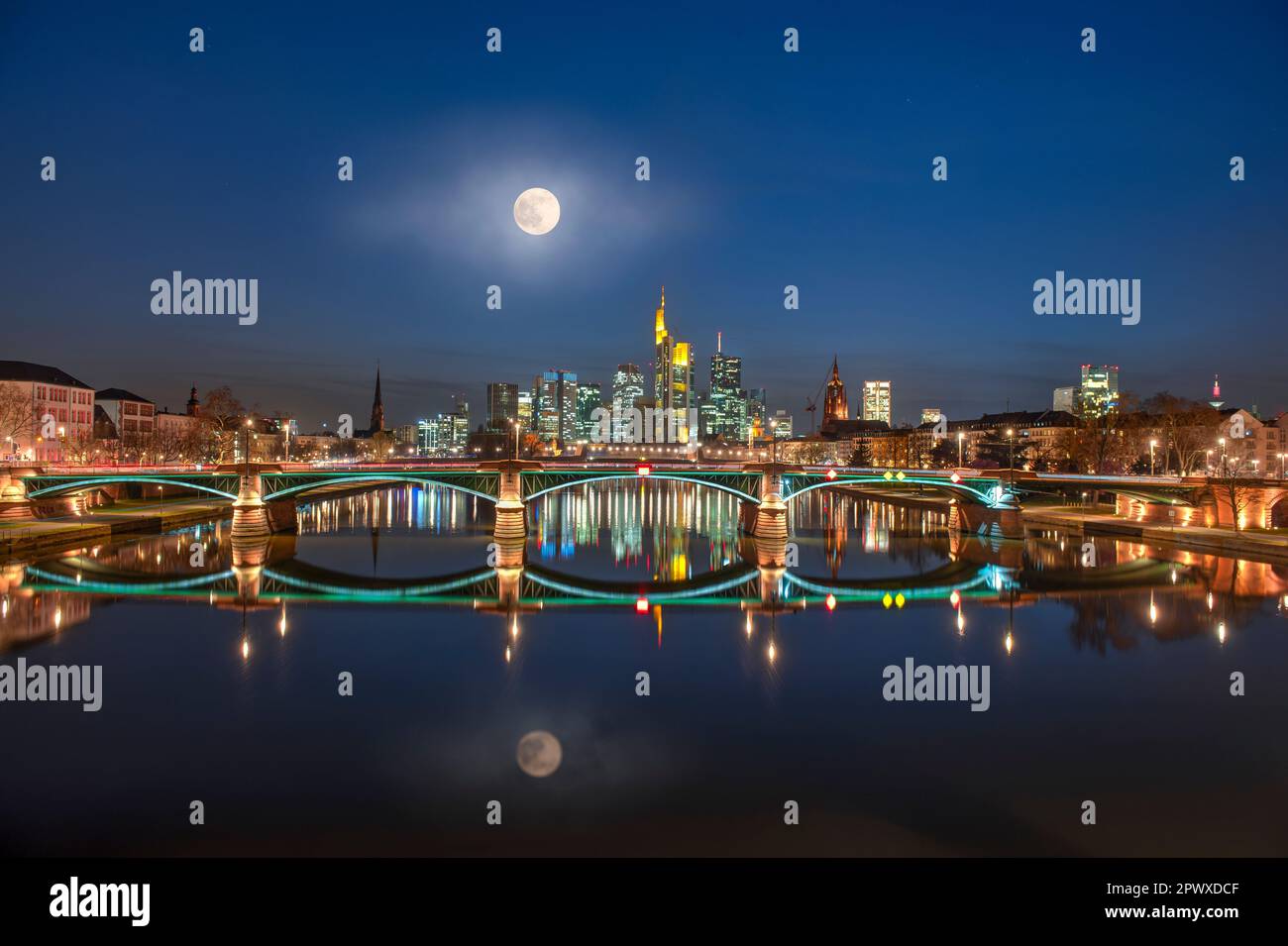 La luna piena si riflette nel fiume meno con lo skyline serale di Francoforte sul meno illuminato artificialmente Foto Stock