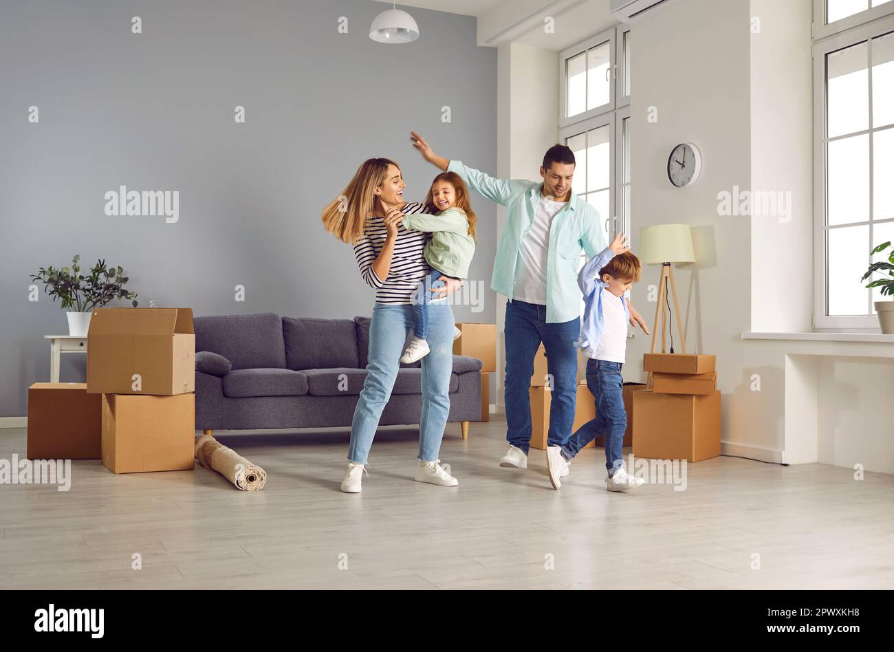 Famiglia felice con due bambini sono felici di trasferirsi in un nuovo appartamento. I giovani genitori amorosi con i loro figli ballano insieme per gioia nel soggiorno Foto Stock