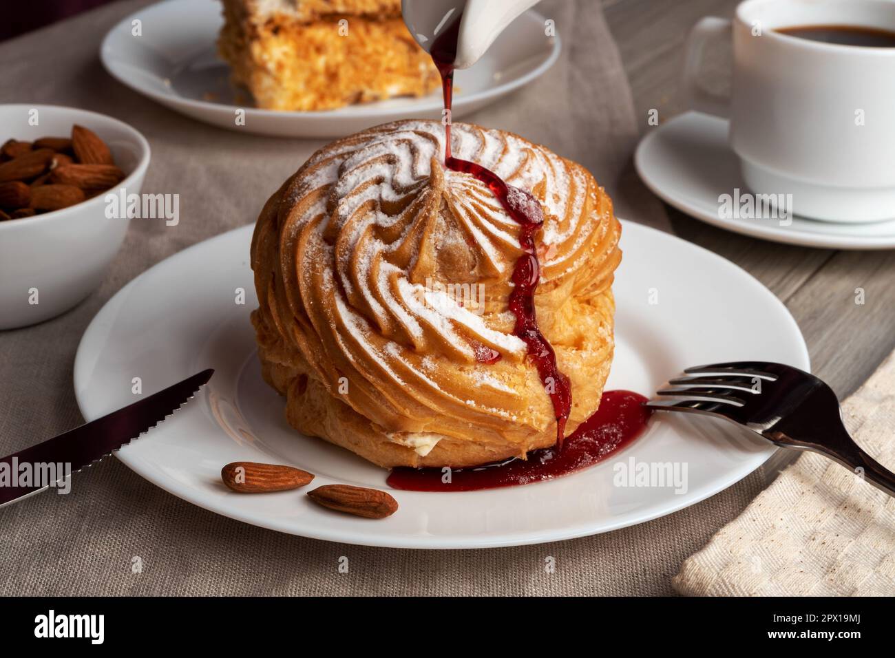 Torta di mandorle profiterole su un piatto con caffè. Dolce delizioso con sciroppo di bacche. Foto Stock