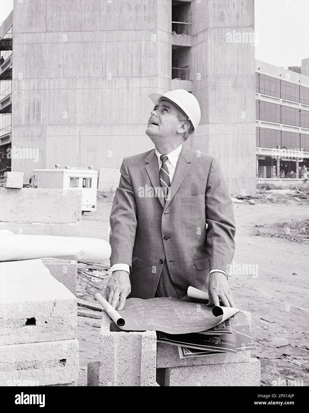 1970S UOMO D'AFFARI BEN VESTITO IN CANTIERE CON BLUEPRINTS CHE INDOSSANO IL CAPPELLO DURO CERCANDO ARCHITETTO BUILDER - I5956 HAR001 HARS LUOGO COPIA SPAZIO PERSONE DI MEZZA LUNGHEZZA MASCHI RISCHIO ARCHITETTO EDIFICI PROFESSIONE BLUEPRINTS BUILDER B&W DI MEZZA ETÀ UOMO DI MEDIA ETÀ OBIETTIVI ABILITÀ TUTA E LEGAME DI OCCUPAZIONE COMPETENZE PROPRIETÀ CARRIERE LEADERSHIP ESTERNA DIREZIONE ORGOGLIO DI OCCUPAZIONE OCCUPAZIONI IMMOBILIARI STRUTTURE DI CONNESSIONE ELEGANTE EDIFICIO NERO E L'ETNIA CAUCASICA BIANCA HAR001 VECCHIO STILE Foto Stock