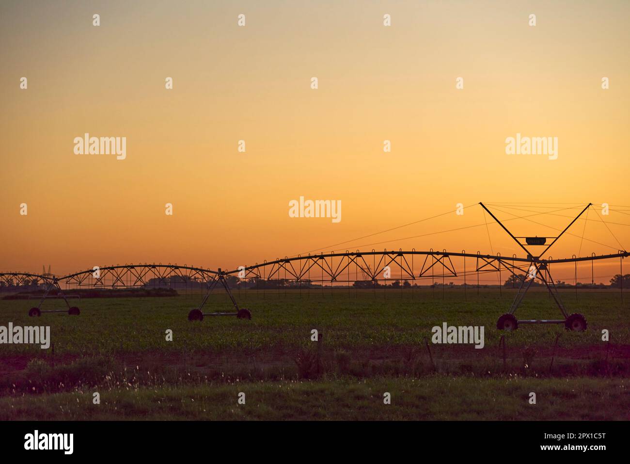 Agricoltura in Argentina: Tramonto in campagna, contro un cielo arancione, la sagoma di un sistema di irrigazione agricola in controluce. Foto Stock