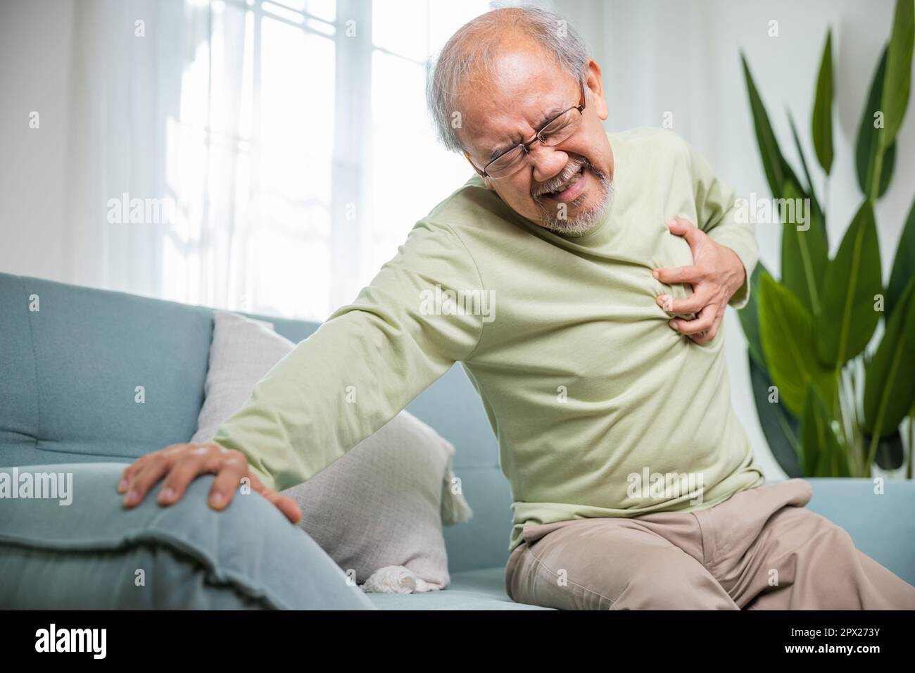 Uomo anziano mal di mano che tocca il petto con attacco di cuore, l'uomo anziano asiatico hanno malattia congenita che soffre di dolore cardiaco solo a casa il suo cuore Foto Stock