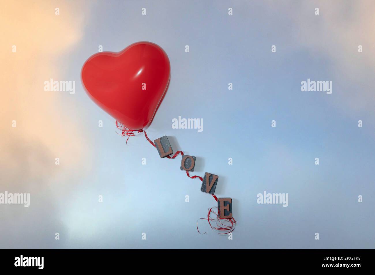 Palloncino a forma di cuore rosso e cordicella rossa con lettere per la parola amore su sfondo azzurro Foto Stock