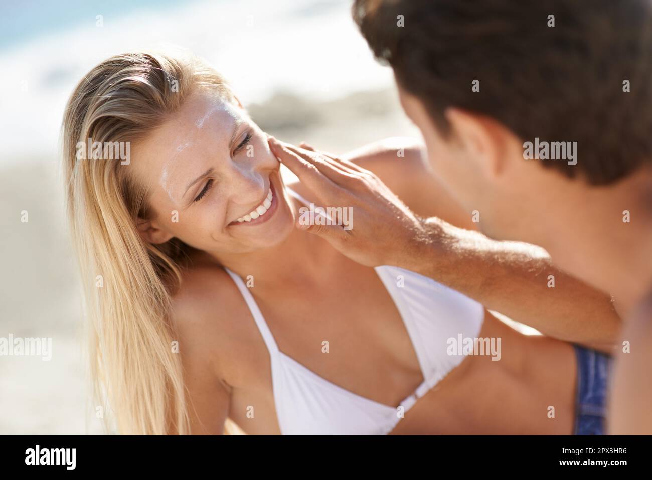 Divertimento con la crema solare. Una giovane coppia che applica crema solare in spiaggia. Foto Stock
