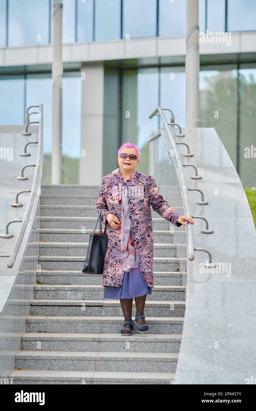 Donna vecchia con capelli rosa in cappotto di cashmere e borsa a mano che  scende le scale Foto stock - Alamy