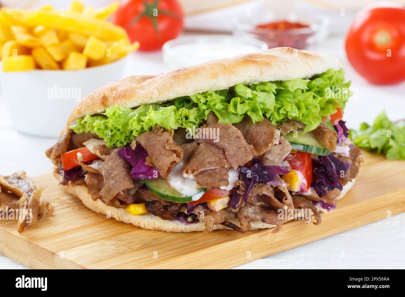 Döner Kebab Doner Kebap pasto fast food in pane piatto con patatine fritte su uno spuntino con tavola di legno Foto Stock