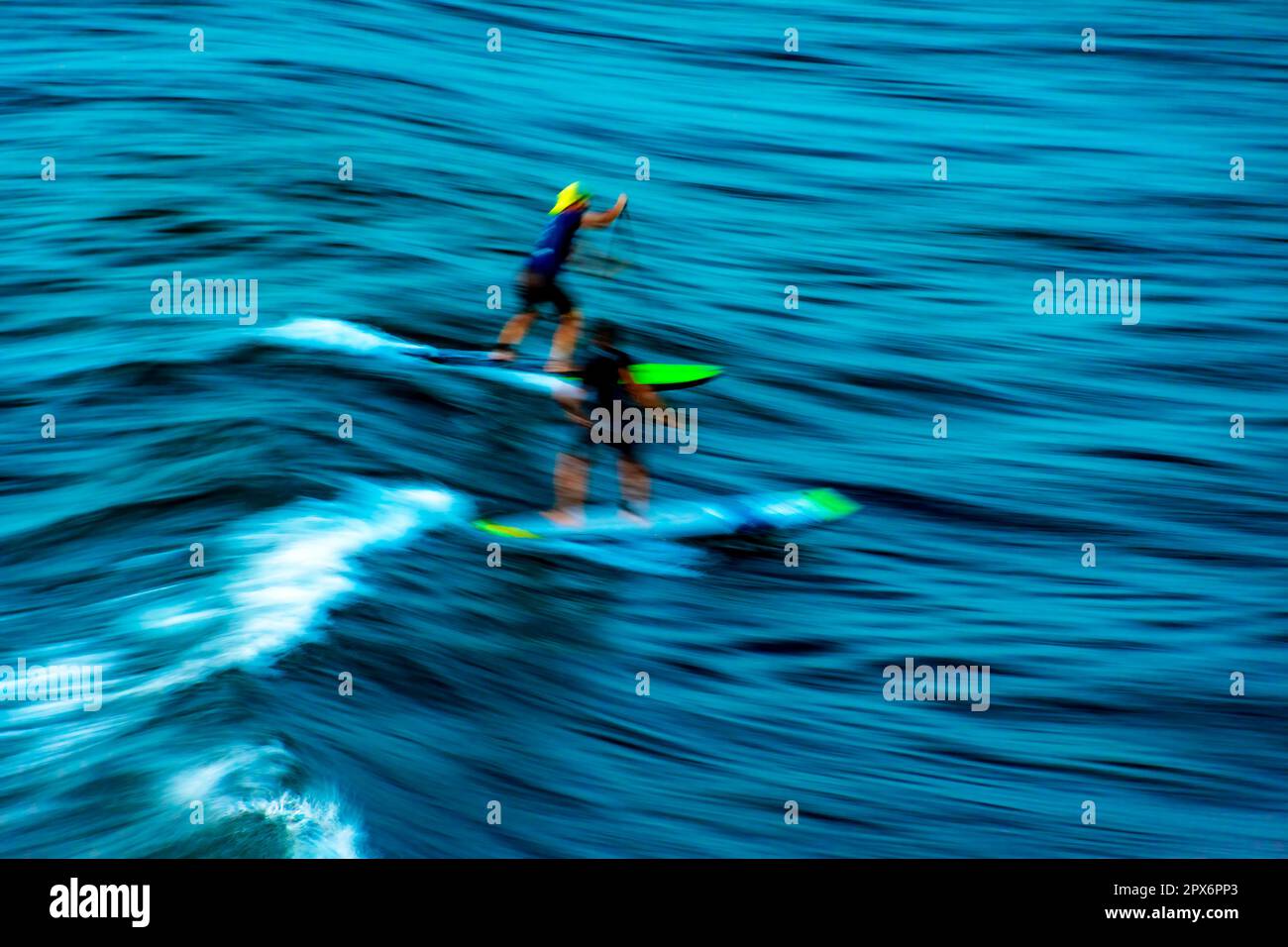 Alzati a pagaiare sulle onde al tramonto nel mare della città di Salvador a Bahia con movimento sfocato e persone irriconoscibili Foto Stock