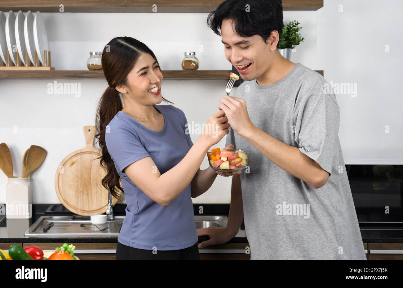 Coppie asiatiche trascorrono del tempo insieme in cucina. Giovane donna nutrire il suo ragazzo un pezzo di mela da insalata ciotola. Foto Stock