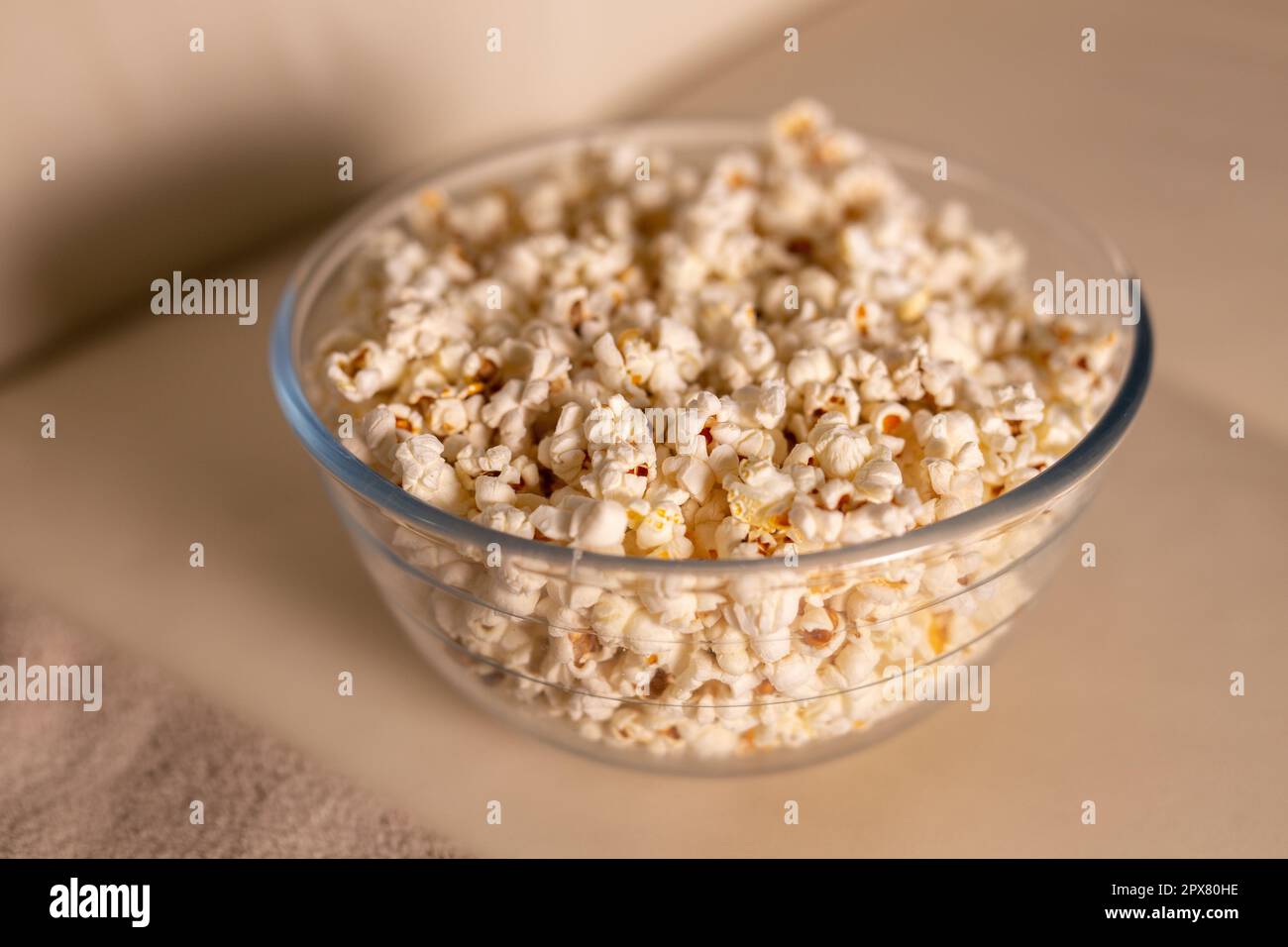 Ciotola di popcorn per guardare un film su un divano beige. Spuntini e cibo spazzatura malsano. Foto Stock