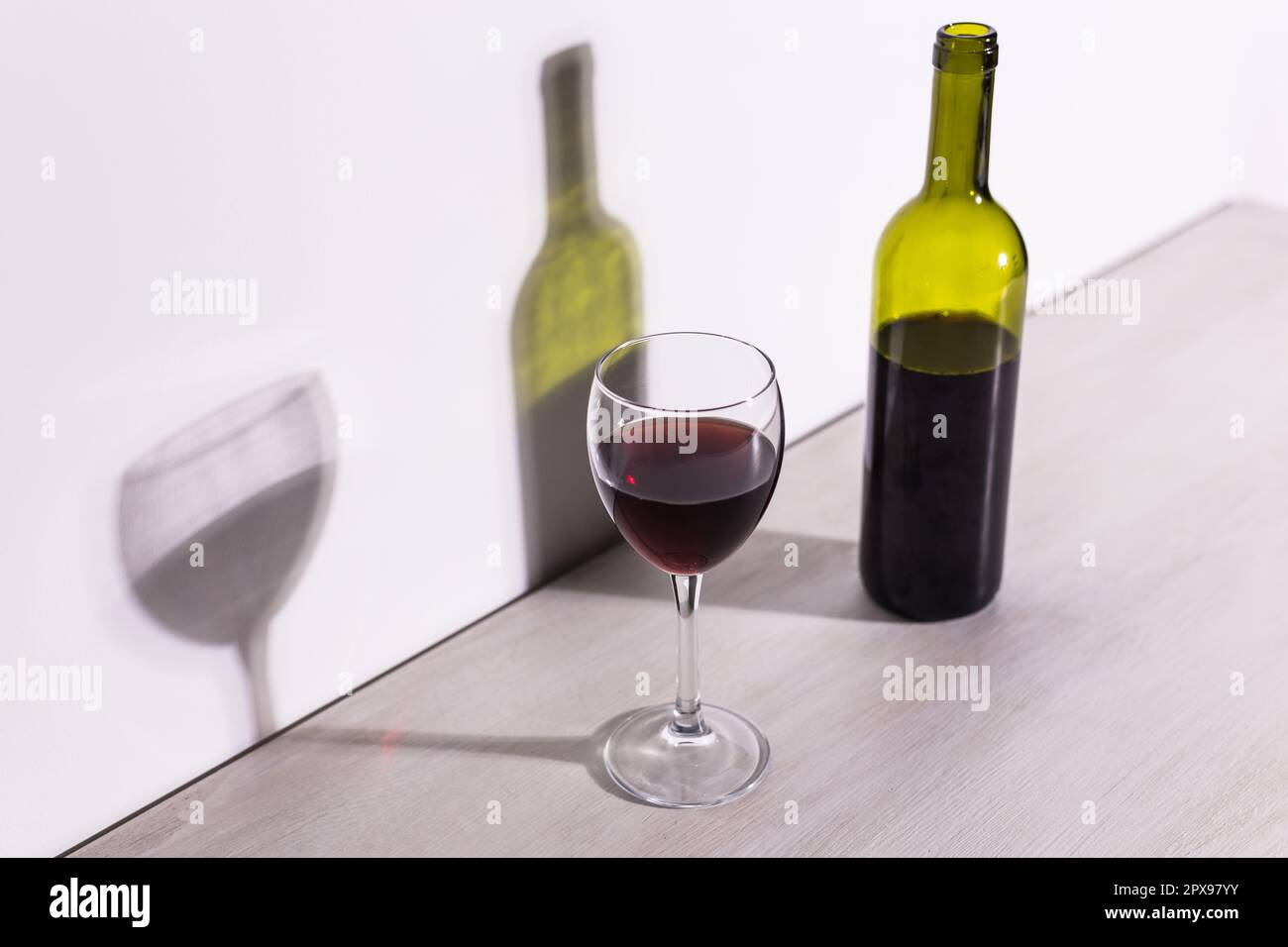 Un bicchiere di vino e una bottiglia getta una lunga ombra dal sole della  sera Foto stock - Alamy