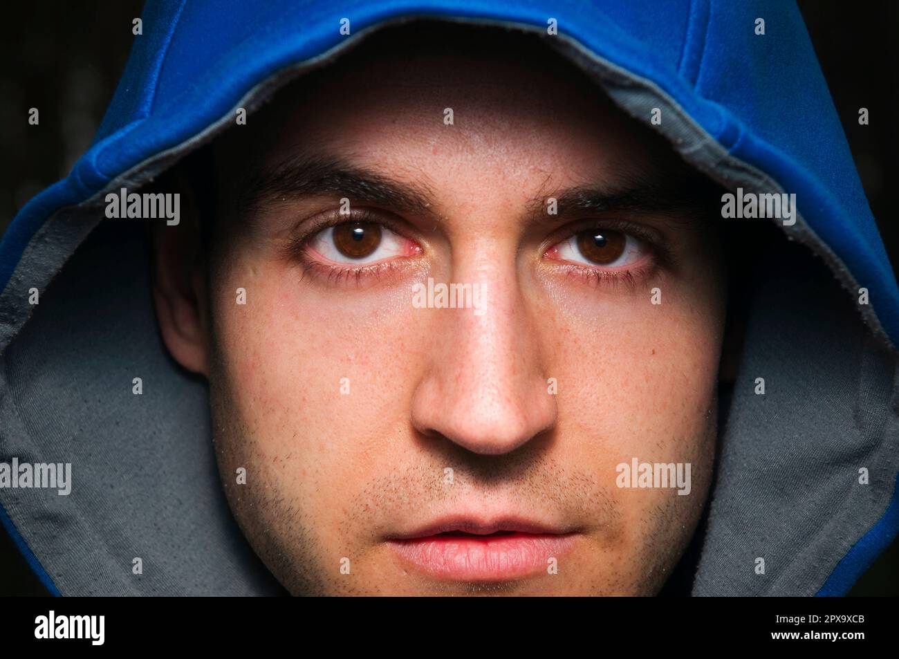 Ritratto frontale di un giovane uomo con cappuccio blu che guarda direttamente e con pietà la fotocamera. Foto Stock