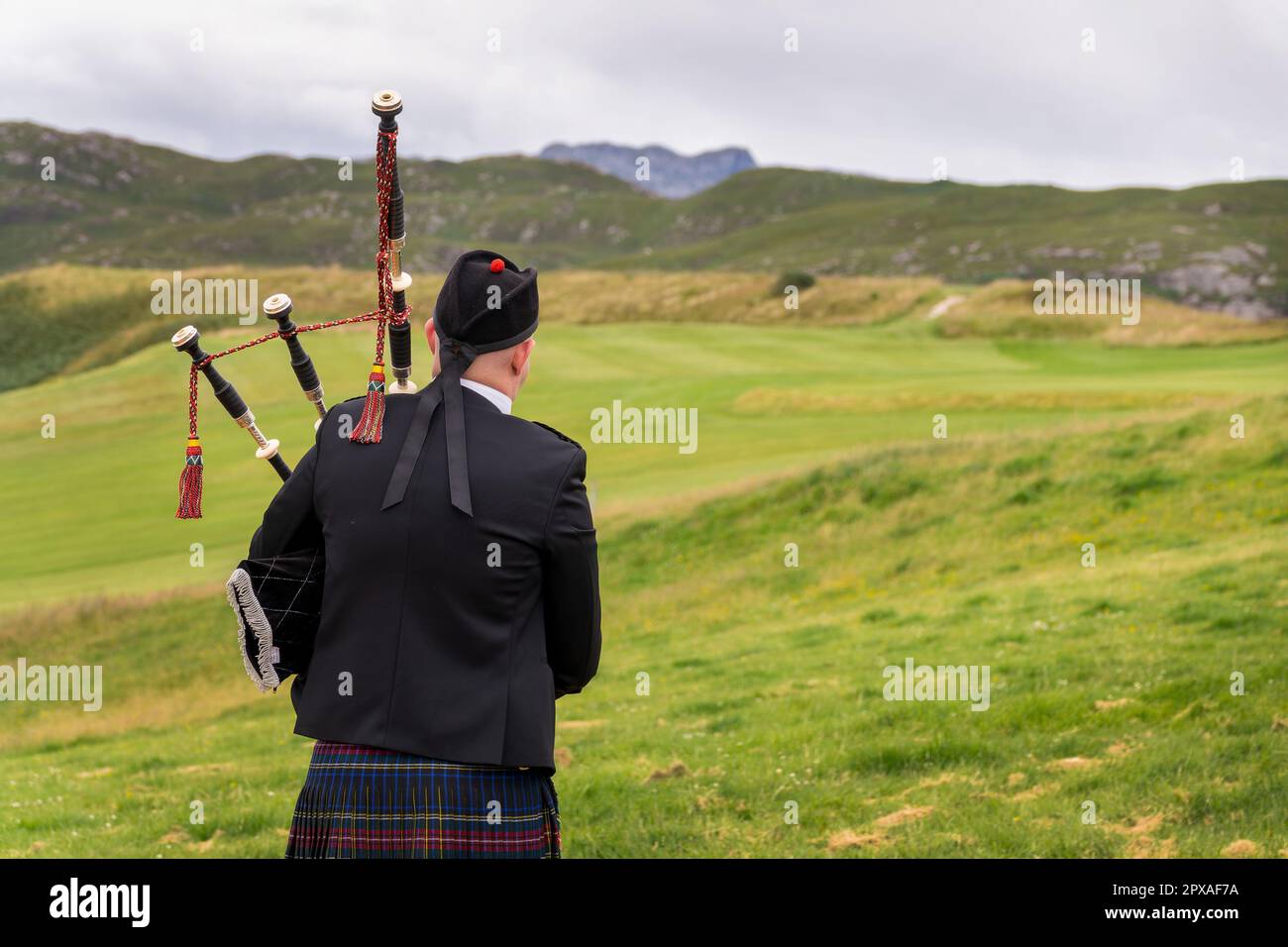 Retro di un bagpiper scozzese nelle Highlands della Scozia, montagne sullo sfondo, Regno Unito Foto Stock