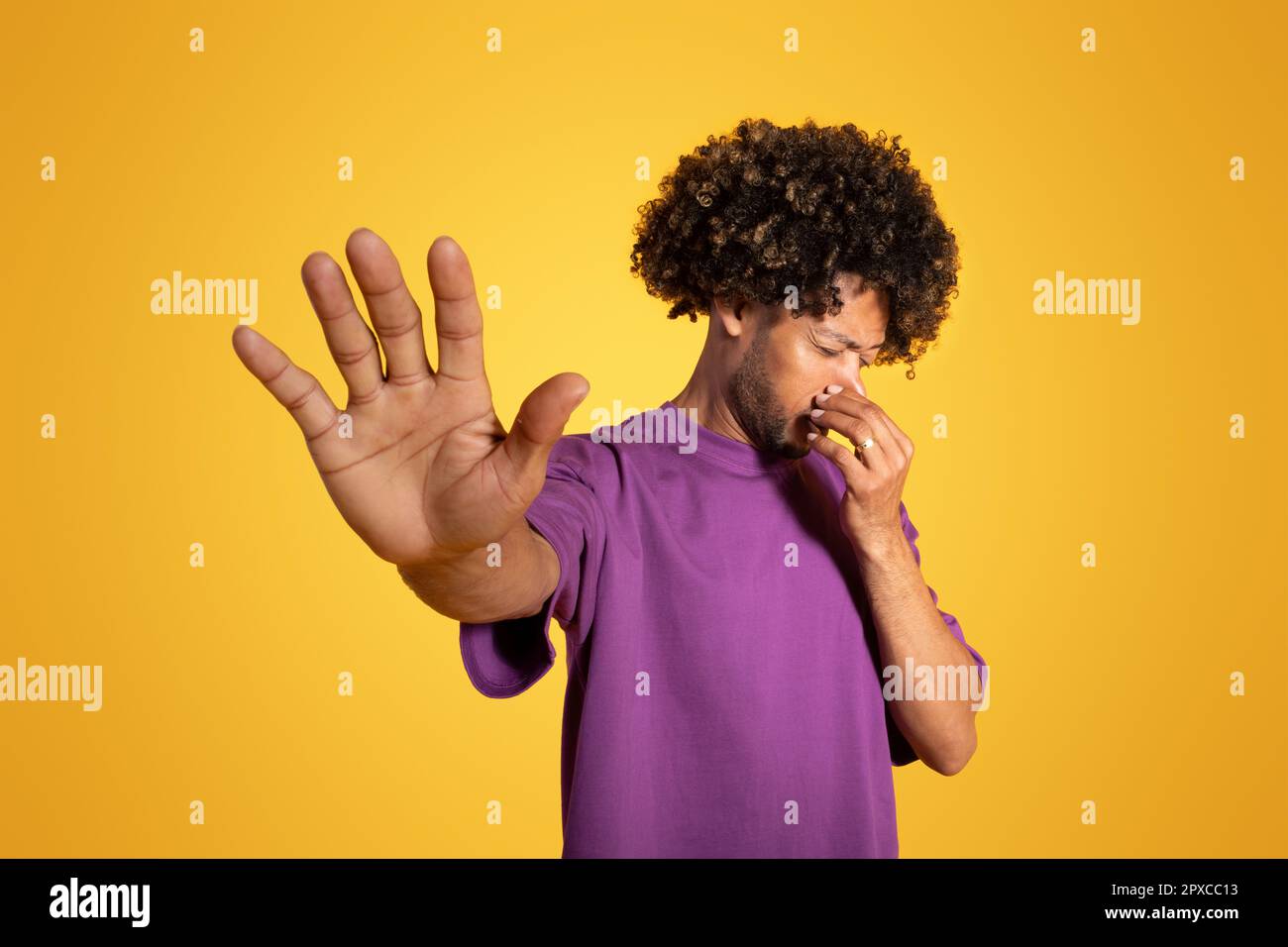 Infelice uomo afroamericano in t-shirt viola che copre il naso, facendo segno di stop Foto Stock