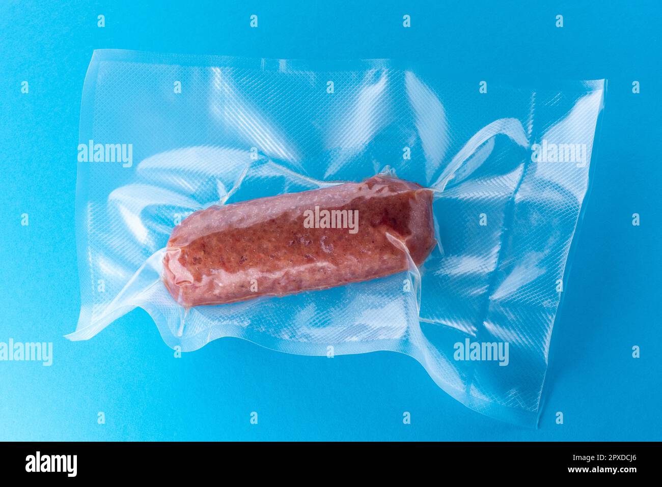 Cotechino italiano in confezione sottovuoto per cucinare sous vide su sfondo blu Foto Stock