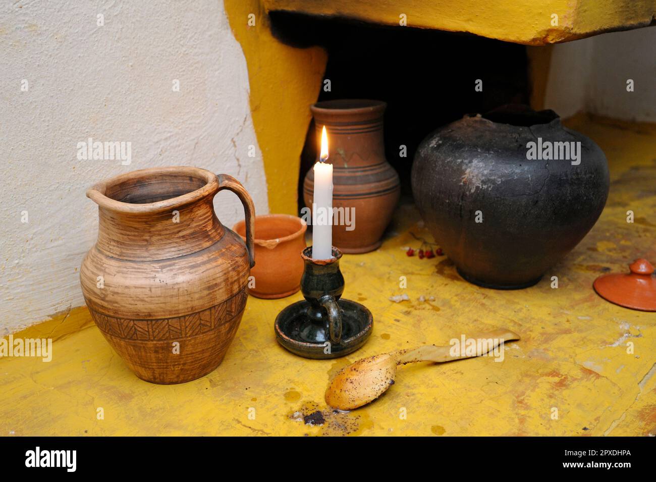 Tradizionale ucraino creta, vaso, cucchiaio di legno e candela bruciante posto vicino vecchio forno rustico. Kiev, Ucraina Foto Stock