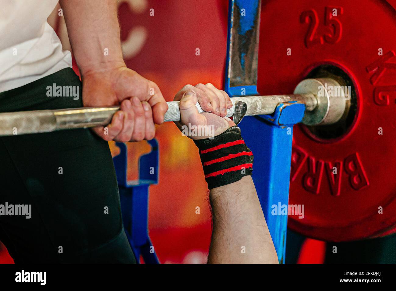 mano maschio powerlifter che tiene il barbell nella pressa del banco, il coach fornisce la concorrenza di powerlifting di supporto Foto Stock