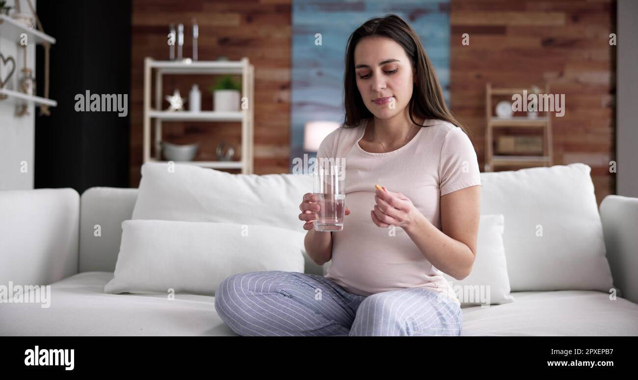 Donna incinta mano con un bicchiere di acqua e vitamina pillola Foto Stock