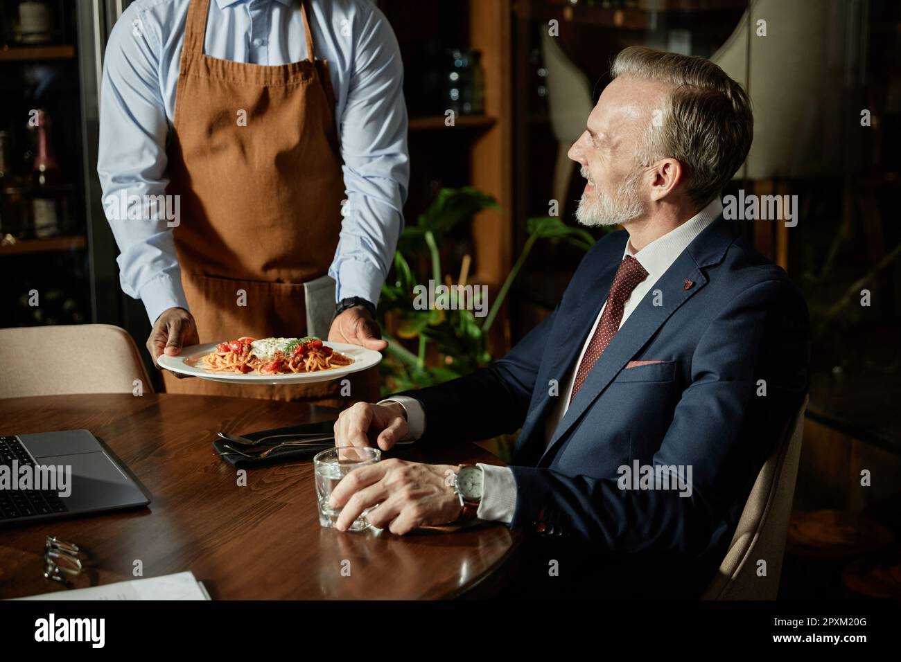 Il cameriere serve cibo per un uomo d'affari mentre si siede al tavolo durante il pranzo al bar Foto Stock