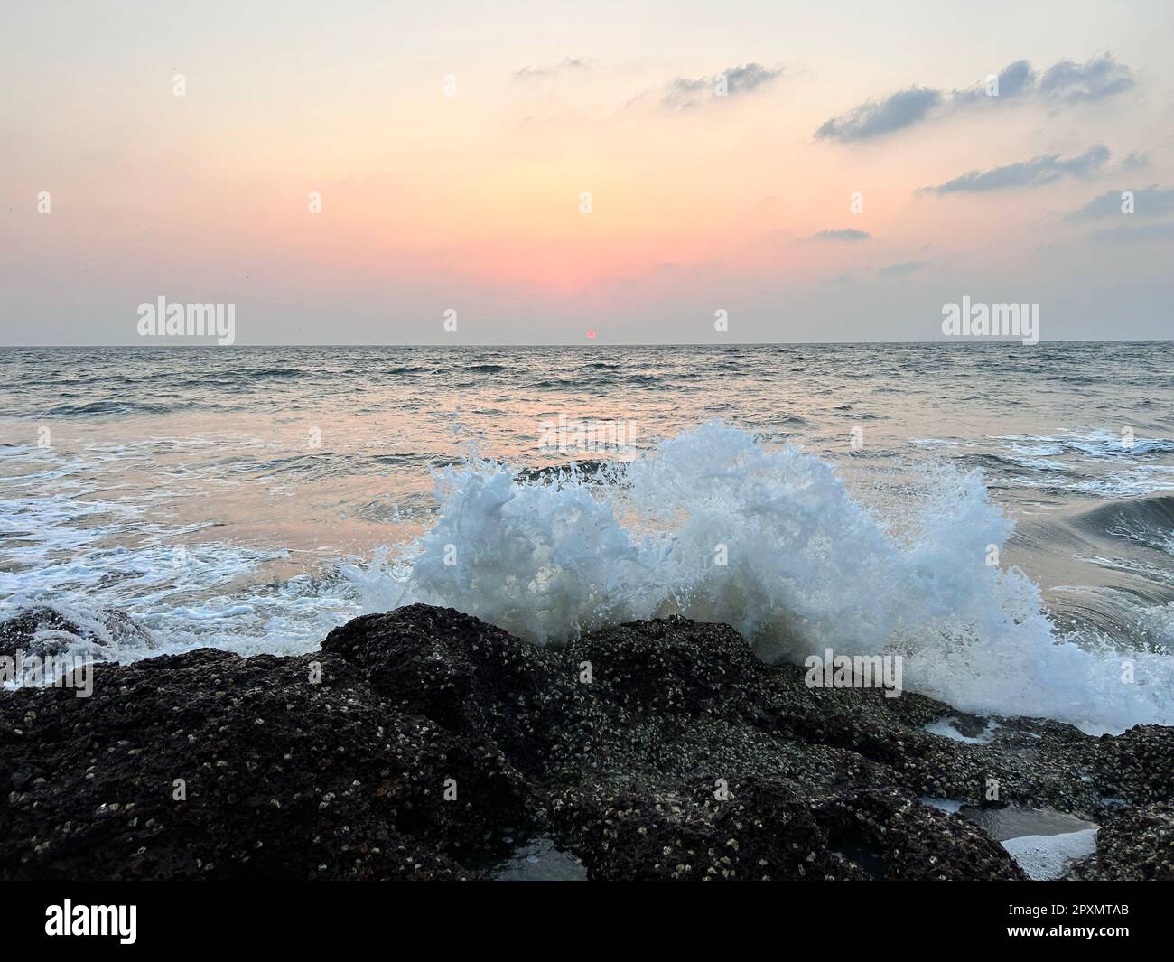 Una tranquilla onda dell'oceano si affaccia sulla costa rocciosa al tramonto, creando una scena rilassante e tranquilla Foto Stock