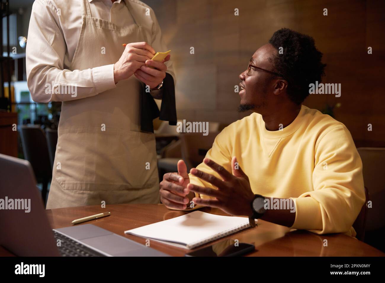 Un uomo d'affari afroamericano che fa ordine al cameriere mentre si siede al tavolo durante il pranzo nel cafè Foto Stock