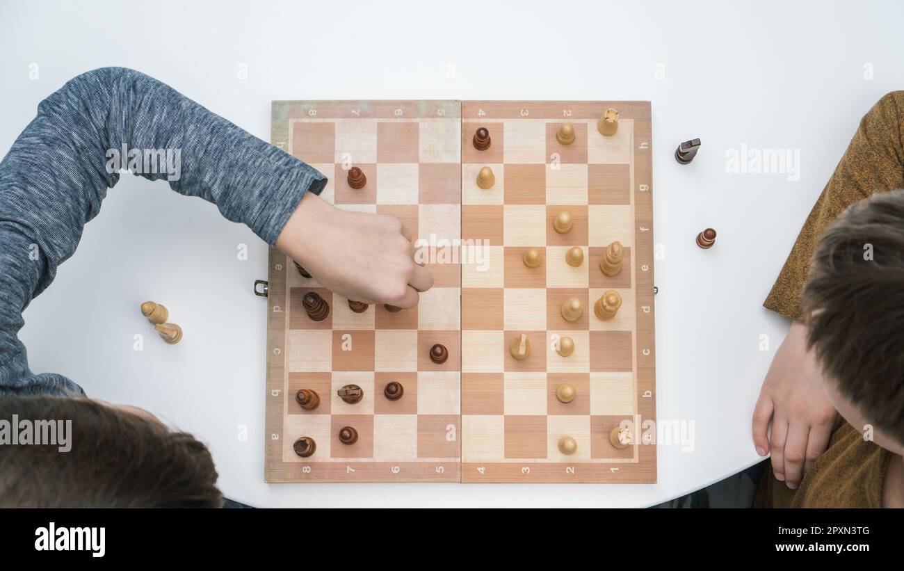 Vista dall'alto di due amici premurosi, fratelli seduti a un tavolo bianco, giocare a scacchi su una tavola di legno, pensare, costruire strategia, tenere figu Foto Stock