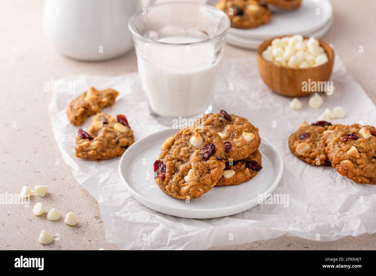 Biscotti al cioccolato bianco e ai mirtilli rossi su un piatto bianco con un bicchiere di latte Foto Stock
